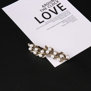 Detail view of the vintage gold leaf hair clip with white pearls on a black background