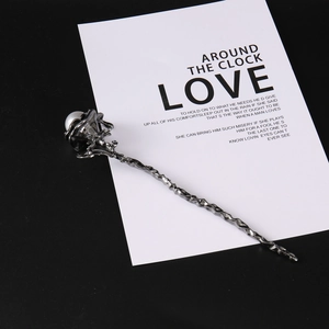 Detail view of the metallic rose hair pin with white pearl accent on a black background