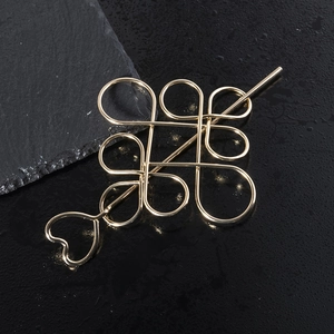 Close-up of golden hollow Chinese knot hair slide and heart-shaped hairpin on black surface