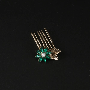 Vintage gold hair comb with green crystal flower and pearl accent on black background