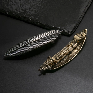 Pair of antique gold and silver metal feather hair clips with detailed texture and spring grip