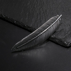 Close-up of vintage silver feather hair clip with intricate metal texture on a slate stone
