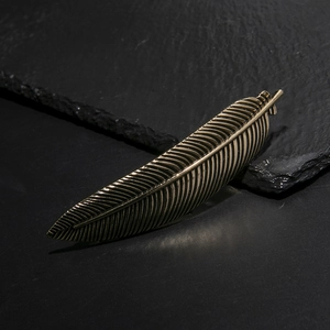 Vintage gold feather hair clip with intricate metal textures on a dark rock background