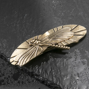 Vintage dragonfly hair clip in embossed brass on textured dark stone background