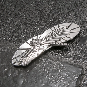 Detailed close-up of a vintage silver dragonfly hairpin on a textured rock background