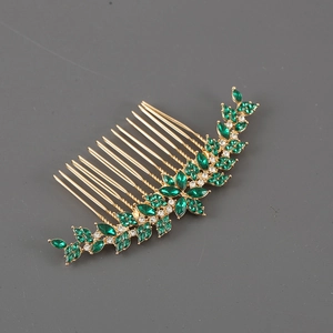 Macro di un pettine per capelli dorato con cristalli verde smeraldo e strass bianchi