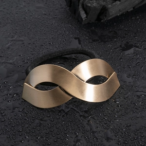 Matte gold infinity metal hair tie with thick black elastic on wet stone background