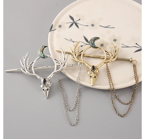 Detail of antler hair pins with crescent moon inlay and tassel chain on ceramic plate