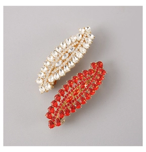 Close-up of golden spring hair clips with white and red crystals in leaf design