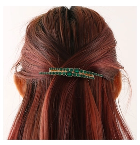 Detailed view of a gold hair clip with green rhinestones styled on red brown hair