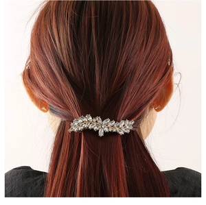 Detail van een sprankelende haarclip in bladvorm met strassteentjes op bruin haar