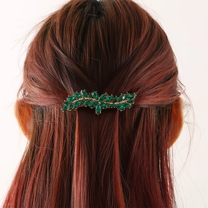 Groene kristallen bladvormige haarclip op bruin haar met een gouden afwerking