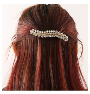 Detailed view of wave-shaped rhinestone hair clip on wavy red brown hair with golden base