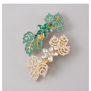 Macro detail of leaf-shaped hair clips featuring emerald green gems and gold plating