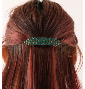 Detail einer eleganten goldenen Haarspange mit grünen Strasssteinen am Haar getragen