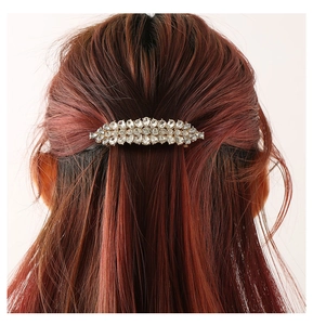 Detailansicht einer goldenen Haarspange mit Kristallsteinen auf langem braunem Haar
