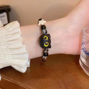 Close-up of black cat charm bracelet with star beads worn on wrist in cozy setting