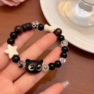 Detail of beaded bracelet with black cat head, white star, and bone charms on wood background