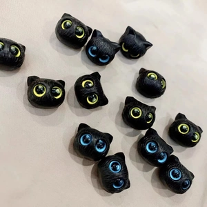 Detailed view of miniature black cat charms with vibrant blue and yellow resin eyes