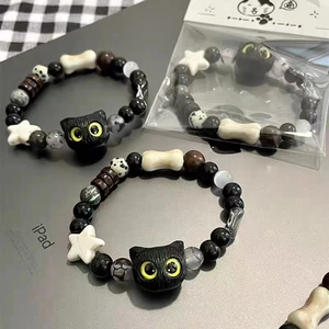 Detail of beaded bracelet with black cat charm, bone accent, and star beads on a grid cloth
