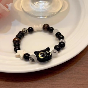 Close-up of black cat charm bracelet with star beads on white ceramic tray