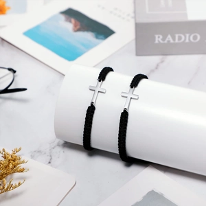 Détail du bracelet tressé noir avec une croix en acier inoxydable poli sur support blanc