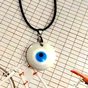 Vista detallada del colgante de ojo turco de cristal con base blanca y cordón negro