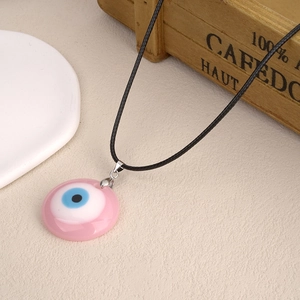 Collar con colgante de ojo turco de vidrio rosa y cordón negro sobre fondo rústico