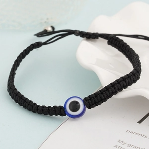 Close-up of black braided evil eye bracelet with blue bead on white shell dish
