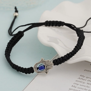 Detail of hand-woven black cord bracelet featuring a silver Hamsa Hand and blue Evil Eye charm