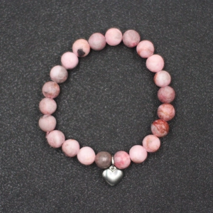 Primer plano de pulsera de cuentas de mármol rosa con dije de corazón plateado en fondo gris