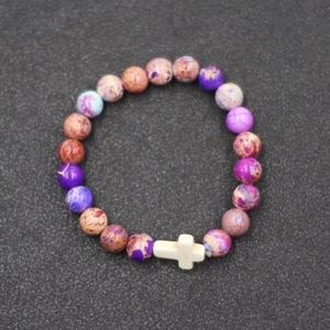 Detalle macro de la pulsera de cuentas de piedra de colores con un dije de cruz blanca