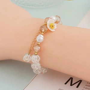 Macro detail of beaded bracelet with white flower charm and golden extension chain