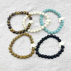 Dettaglio di cinque braccialetti di perline con pietre diverse e ciondoli a delfino bianco