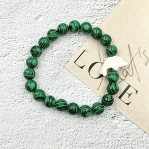 Bracciale di malachite con ciondolo a delfino bianco su superficie di pietra minimalista