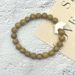 Bracciale elastico con perline marroni effetto legno e un ciondolo a forma di delfino bianco