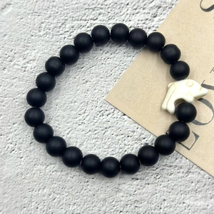 Dettaglio del bracciale con perline nere opache e ciondolo a forma di delfino bianco