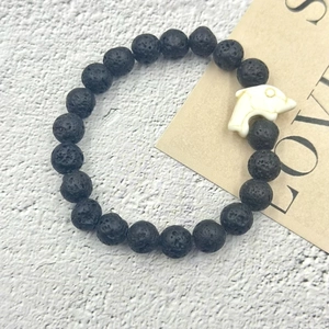 Dettaglio del bracciale in pietra lavica nera con ciondolo a forma di delfino bianco puro