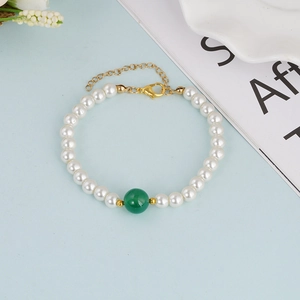 Elegant natural pearl bracelet with green bead accent and gold clasp on blue surface