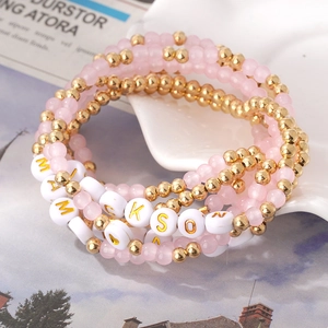Dettaglio di bracciali boho sovrapposti con perle rosa e ciondoli con lettere MAMA