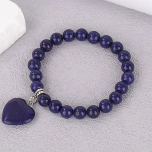 Macro detail of natural lapis lazuli beaded bracelet with a heart pendant on stone background