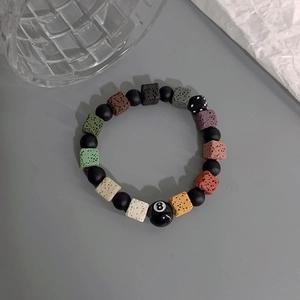 Detail view of volcanic stone bead bracelet with black 8-ball and dice charm