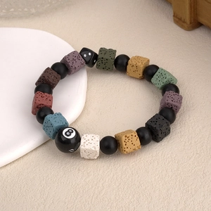 Colorful lava stone bracelet with black 8-ball and dice beads on textured surface