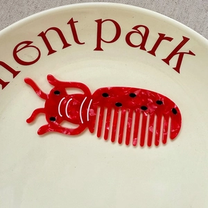 Detail of red marble texture ladybug hair comb made of acetate material on a ceramic plate