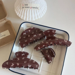 Set of four burgundy hair claws with white butterfly print on white ceramic plate