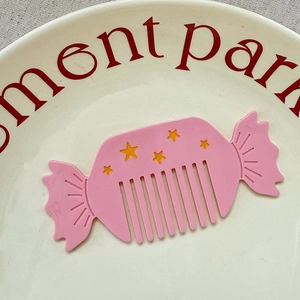 Macro shot of a pink candy-shaped hair comb with yellow stars on a white plate