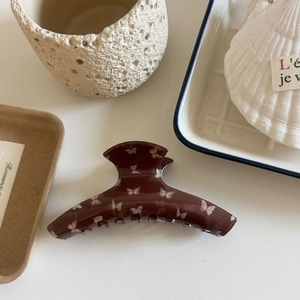 Detail of large dark brown hair claw clip with white butterfly print on ceramic tray