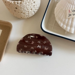 Detailed view of dark brown hair claw with white and pink butterfly print in a lifestyle setting