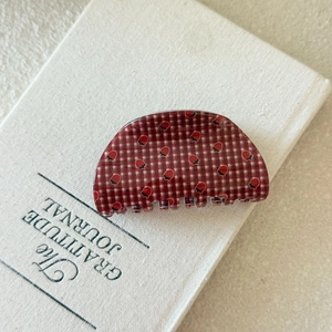 Detailed close-up of large red checkered shark hair claw with strawberry prints on a journal