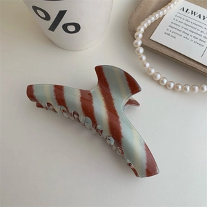 Macro detail of large brown striped cellulose acetate hair claw clip with glossy finish